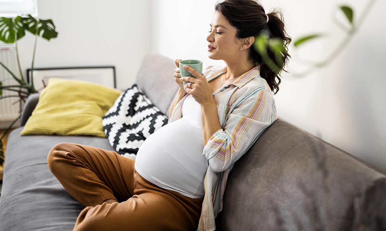 donna in gravidanza siede nel divano sorseggiando una tisana