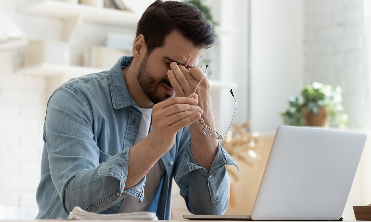 ragazzo davanti al computer si tocca gli occhi per mal di testa