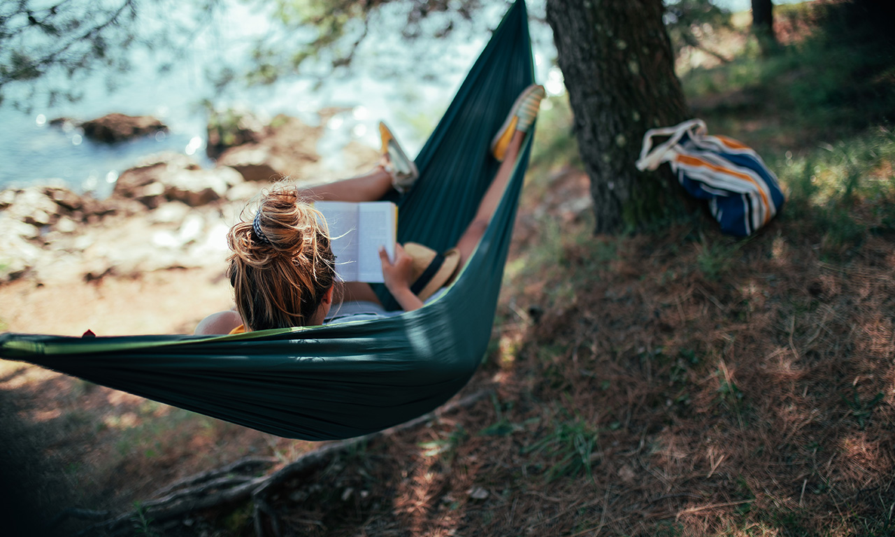 ragazza sull'amaca legge libro sotto un albero vicino al mare